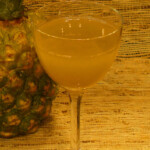 A glass of liquid next to a pineapple.
