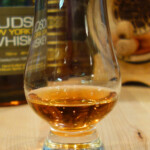 Negroni Barrel Aged White Whiskey Glencairn glass with amber whiskey on wood