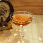 Sherry Aged Gin Wet Martini A glass of whiskey on a table next to a wooden barrel.