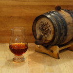 Sherry Cask Aged Bourbon A glass of whiskey next to a wooden barrel.