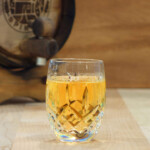 Sherry Aged Gin A glass of whiskey sitting on a table next to a barrel.